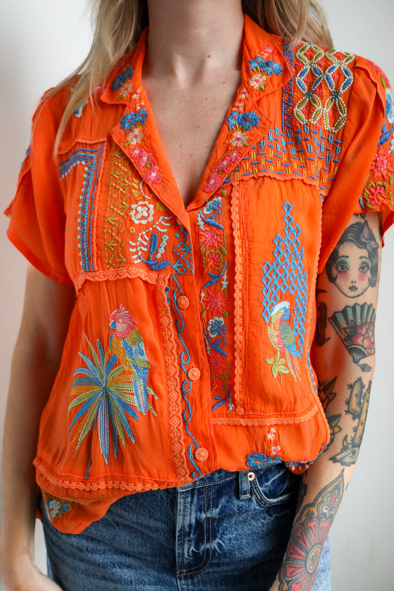 Orange embroidered blouse worn by a person with tattoos on a plain background