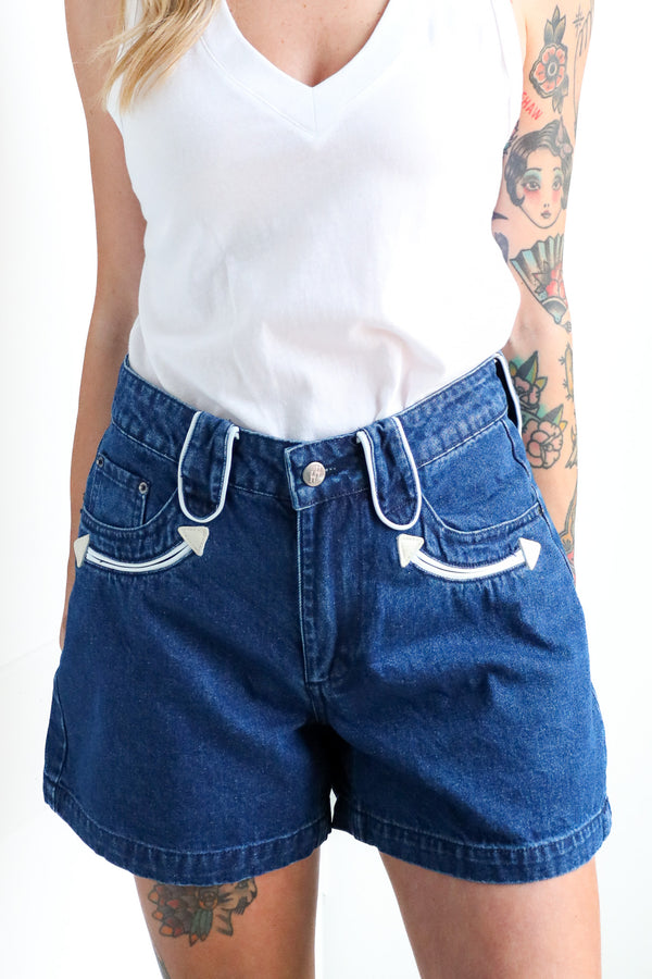 Person wearing blue denim shorts and a white tank top on a plain background
