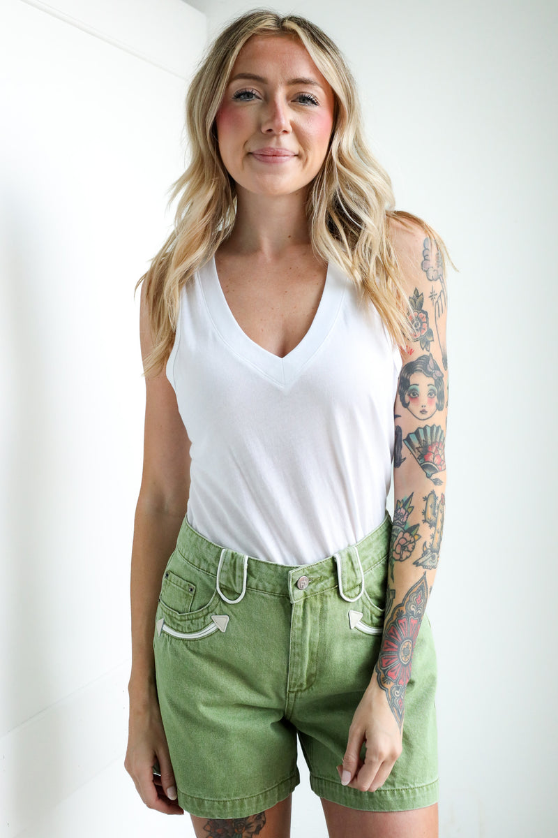 Woman wearing a white tank top and green shorts against a white background