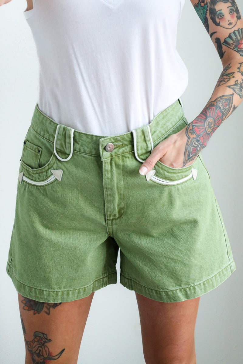 Person wearing green shorts and a white top with tattoos on arms and legs.