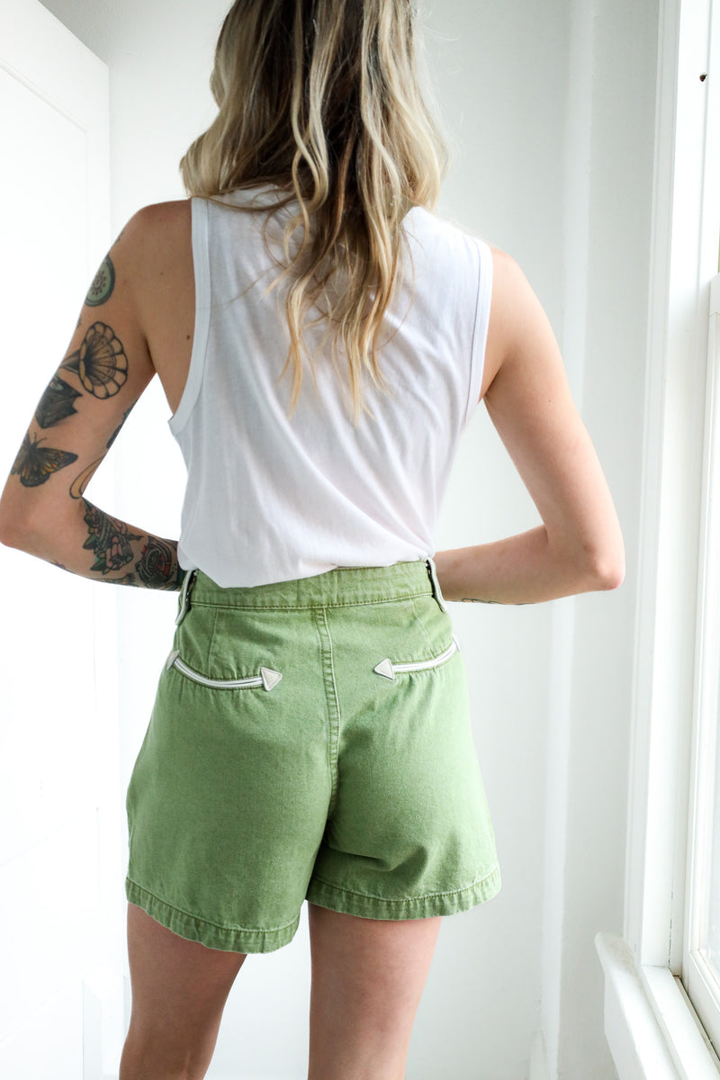 Person wearing a white sleeveless top and green shorts with a plain background