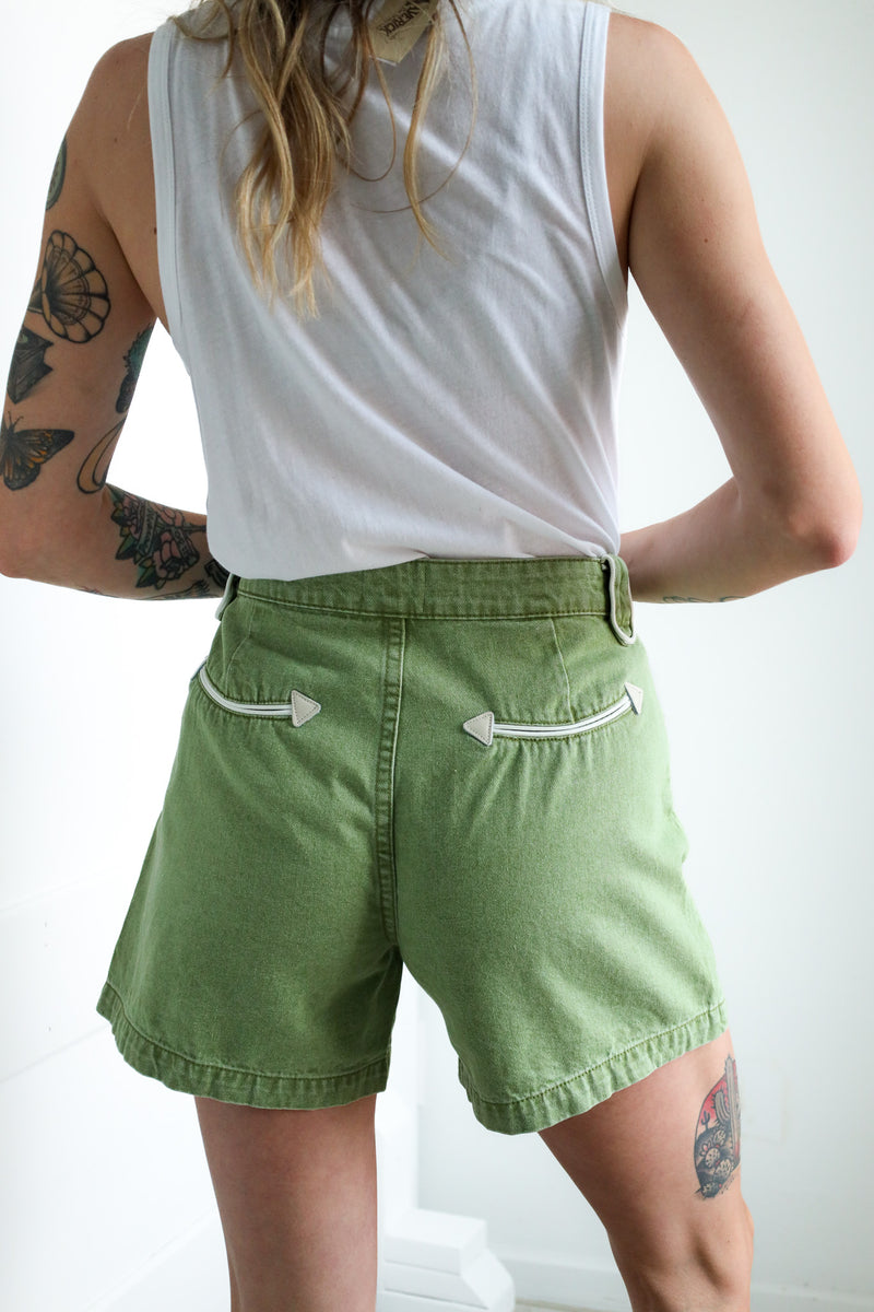 Person wearing green shorts and a white sleeveless top against a plain background