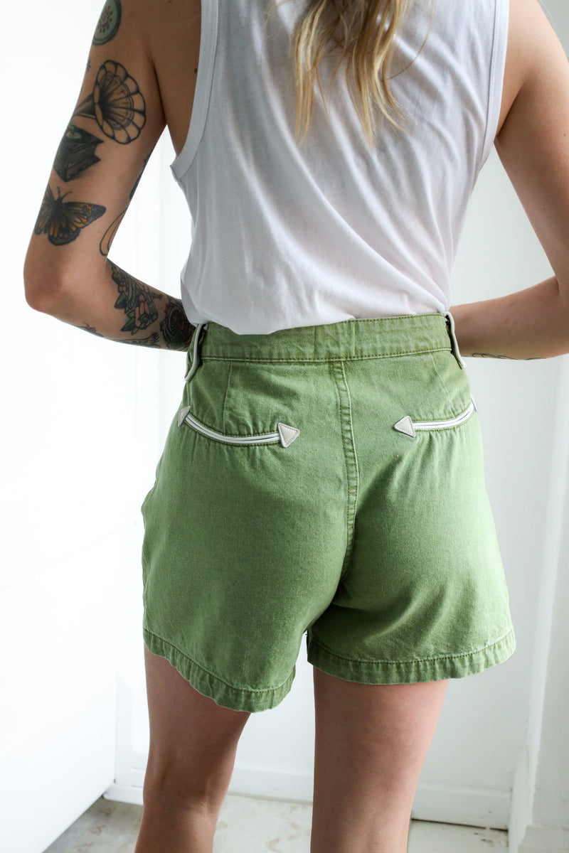 Person wearing green shorts and a white tank top with tattoos on arms.
