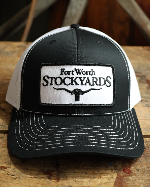 Black and white cap with 'Fort Worth Stockyards' logo on a wooden surface
