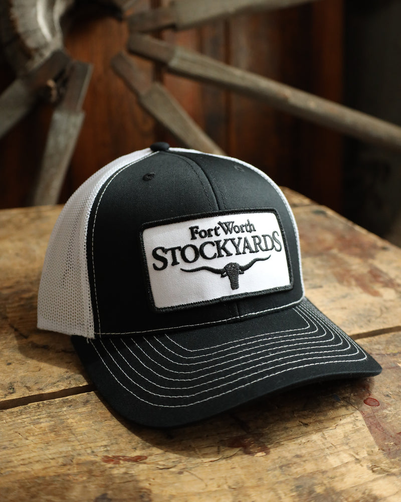 Black and white cap with 'Fort Worth Stockyards' logo on a wooden surface