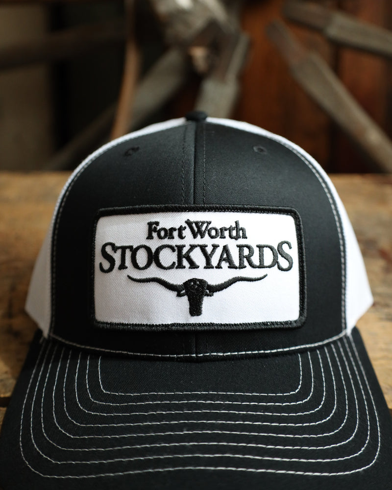 Black and white cap with Fort Worth Stockyards logo on a wooden surface
