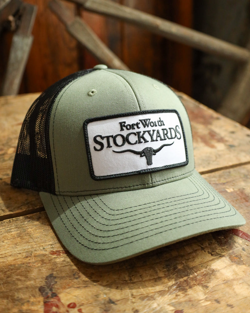 Green trucker hat with 'Fort Worth Stockyards' logo on a wooden surface