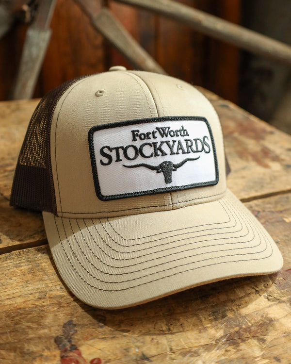 Beige trucker hat with Fort Worth Stockyards logo on a wooden surface