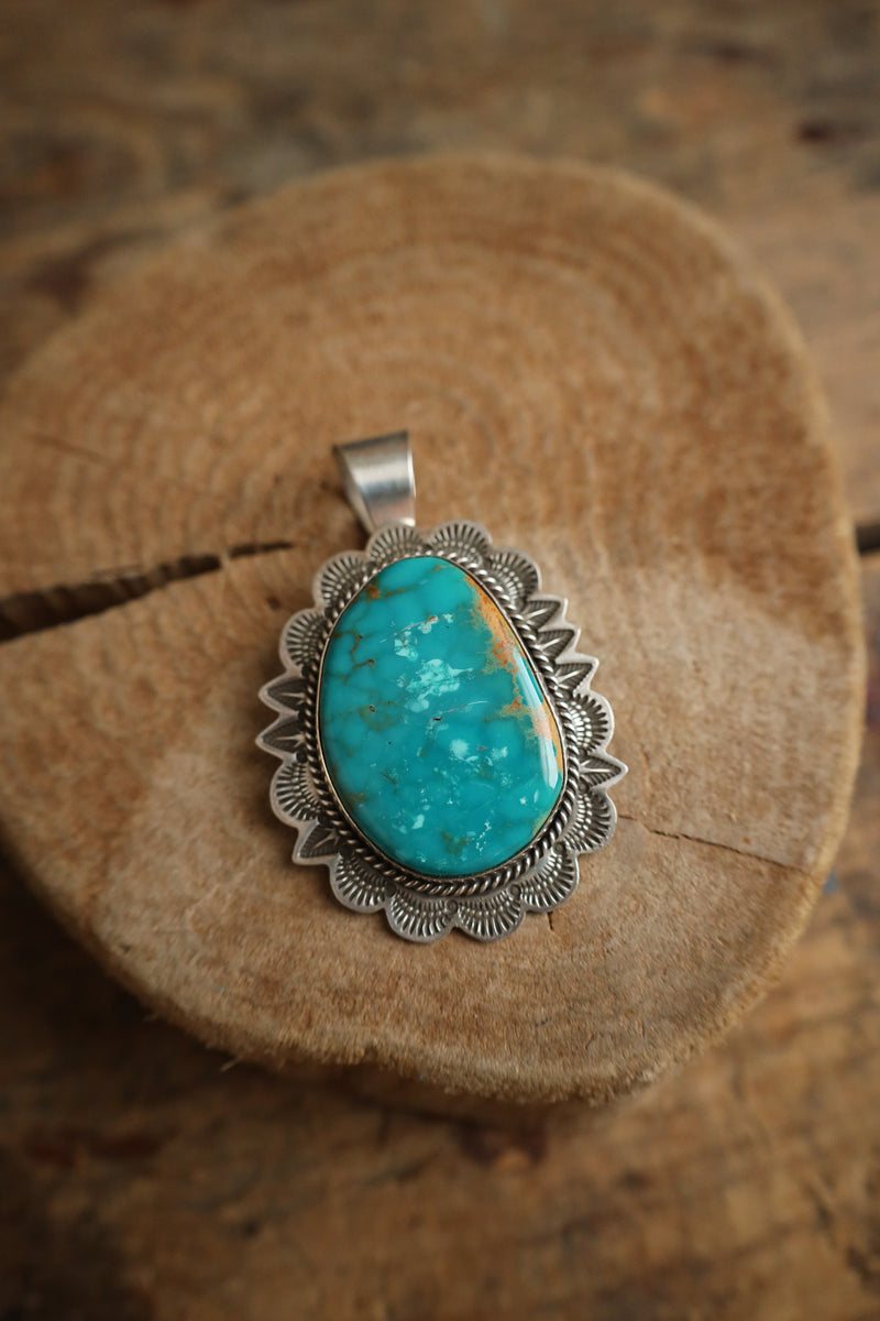 Turquoise stone pendant with silver setting on a wooden surface