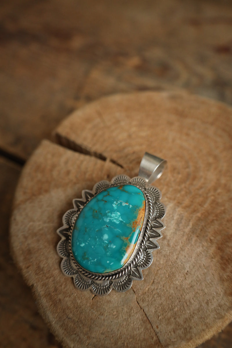 Turquoise stone pendant with silver setting on a wooden surface