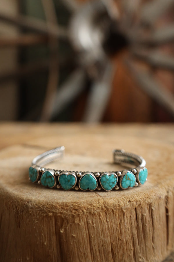 Turquoise heart-shaped stone bracelet on a wooden surface with a blurred background