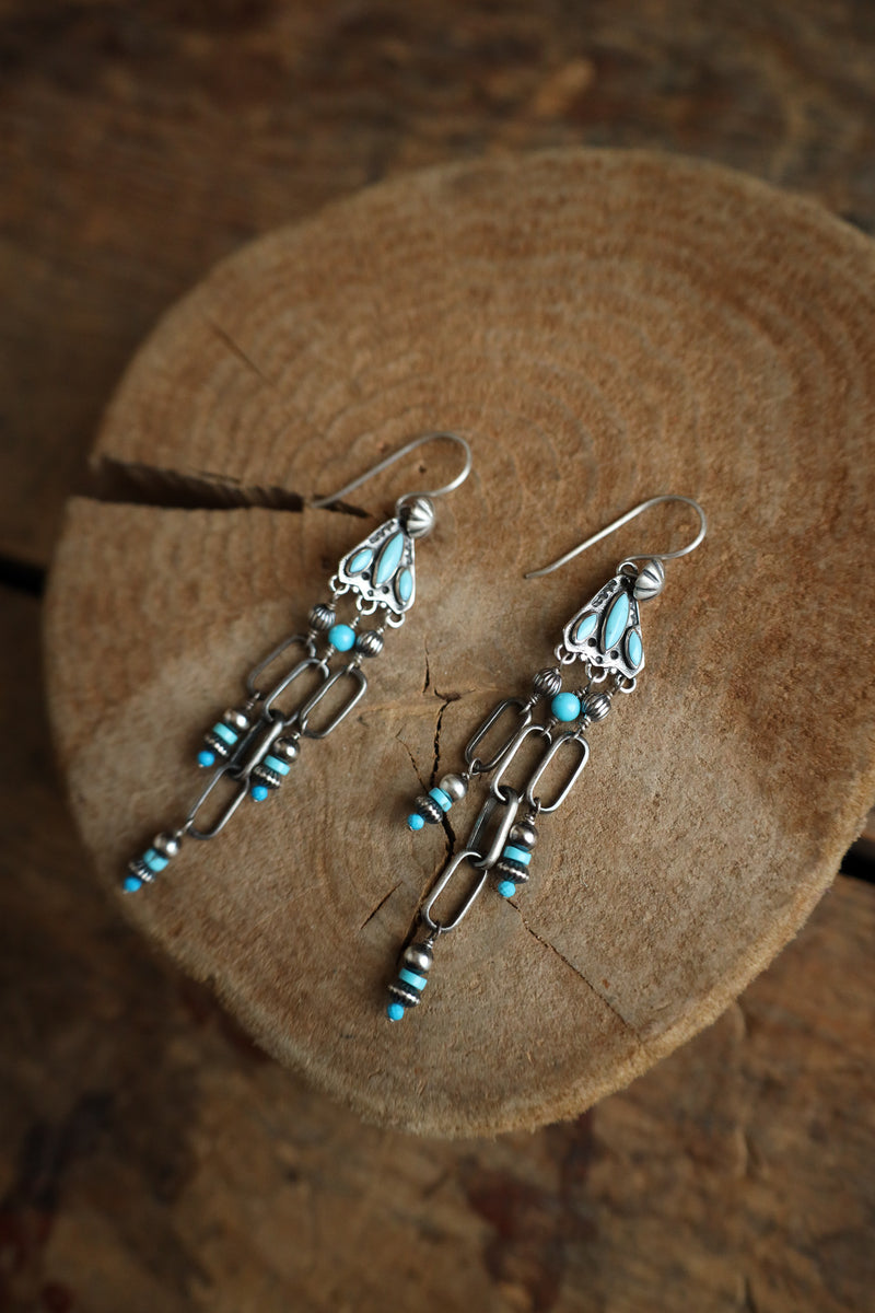 Pair of silver earrings with turquoise beads on a wooden surface