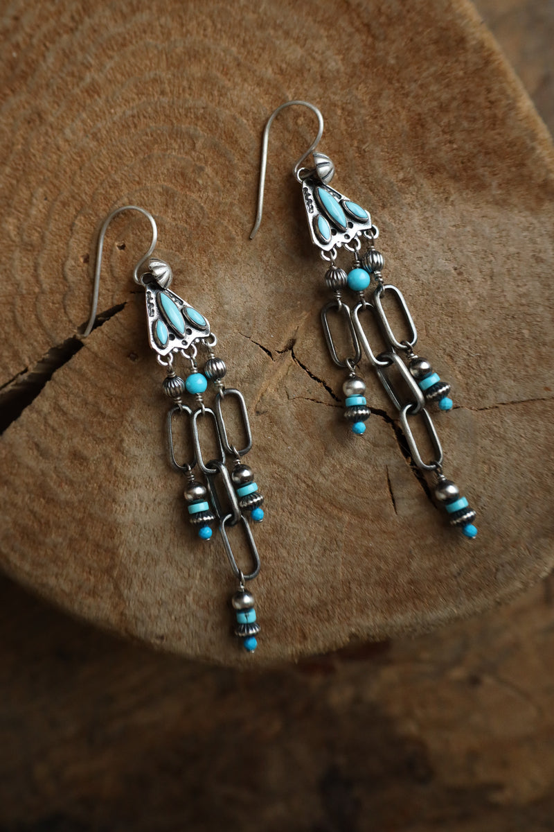 Pair of silver earrings with turquoise beads on a wooden surface