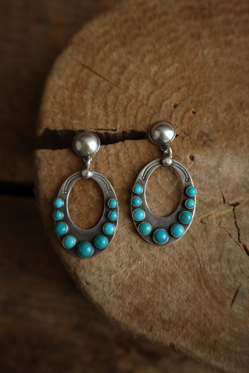 Pair of silver earrings with turquoise stones on a wooden surface