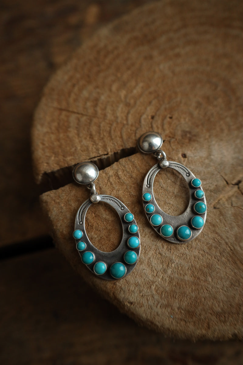 Pair of silver earrings with turquoise stones on a wooden surface