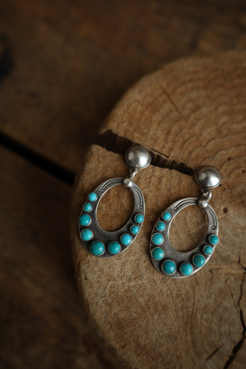 Pair of silver earrings with turquoise stones on a wooden surface