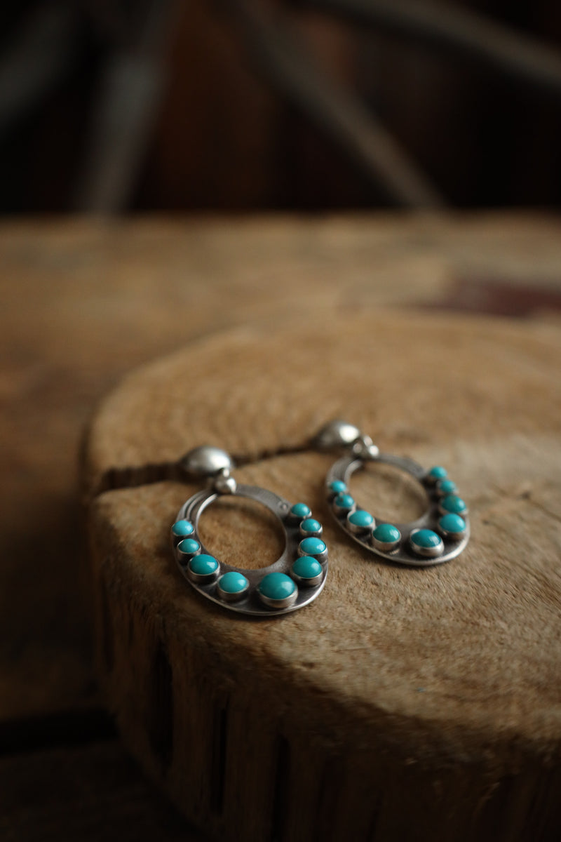 Pair of silver earrings with turquoise stones on a wooden surface