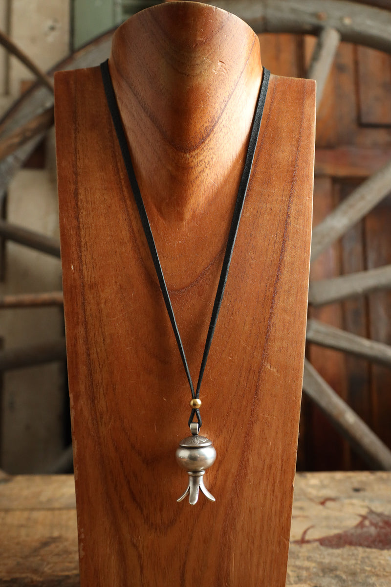 Wooden stand with a necklace featuring a silver pendant and black cord.