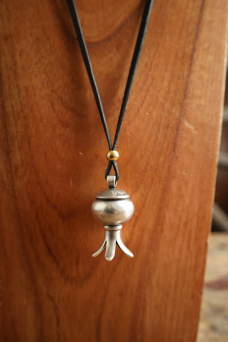 Silver pendant on a black cord against a wooden background