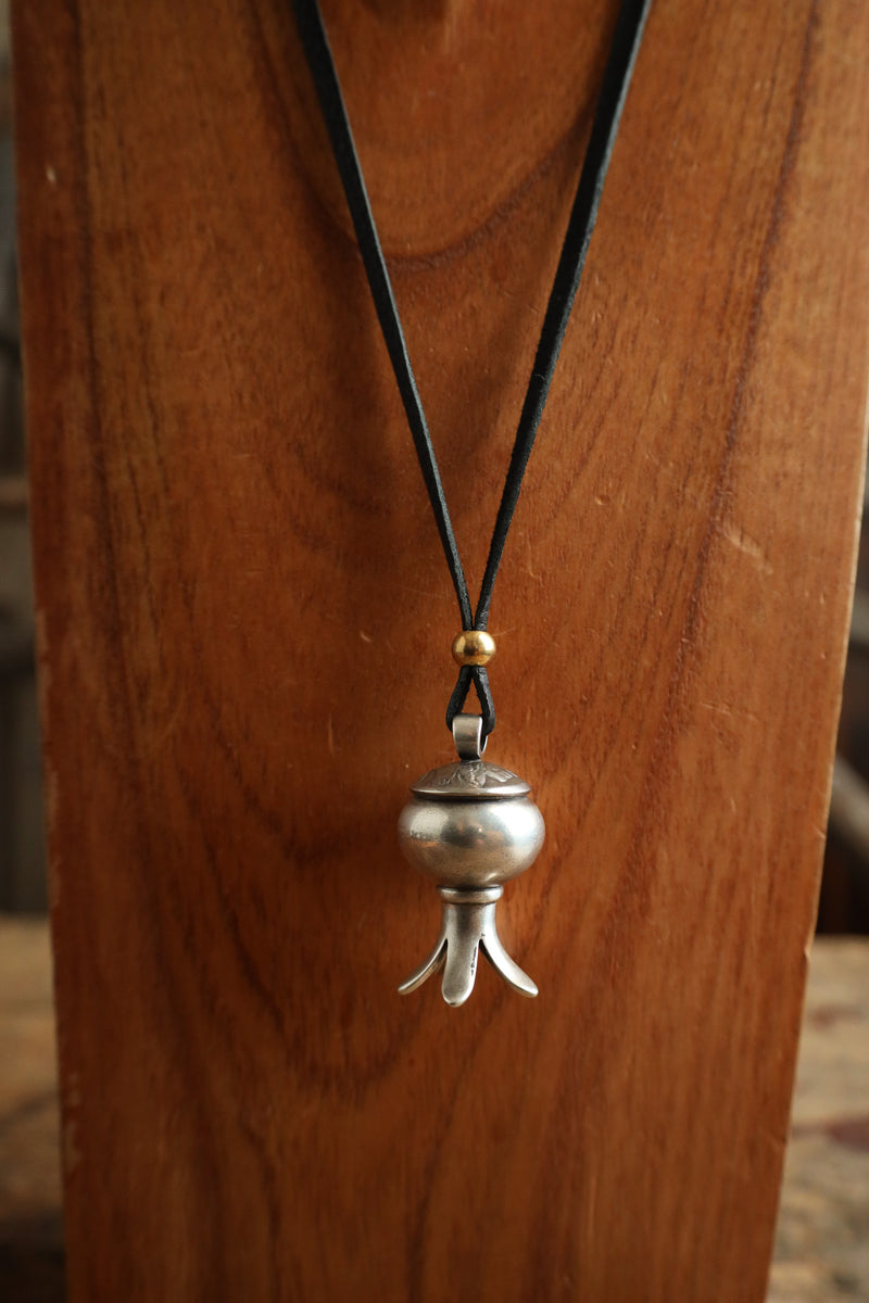 Silver pendant necklace on a black cord against a wooden background