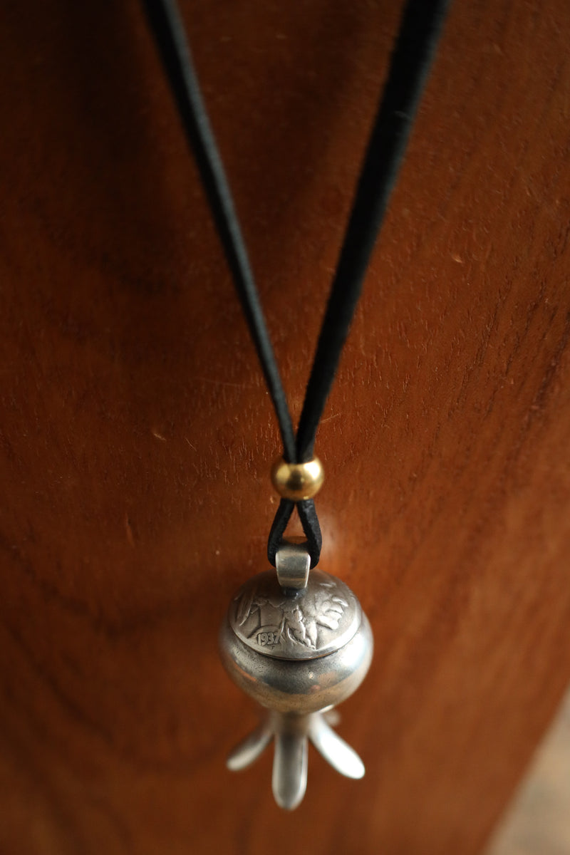 Silver bell pendant on a black cord against a wooden background