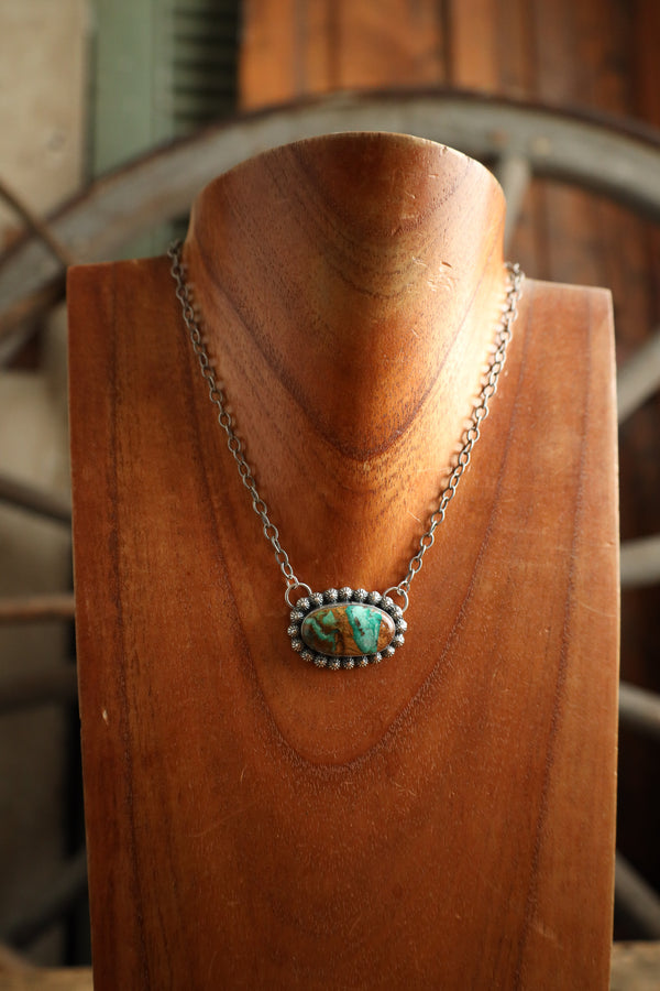 Necklace with a turquoise pendant on a wooden mannequin head.