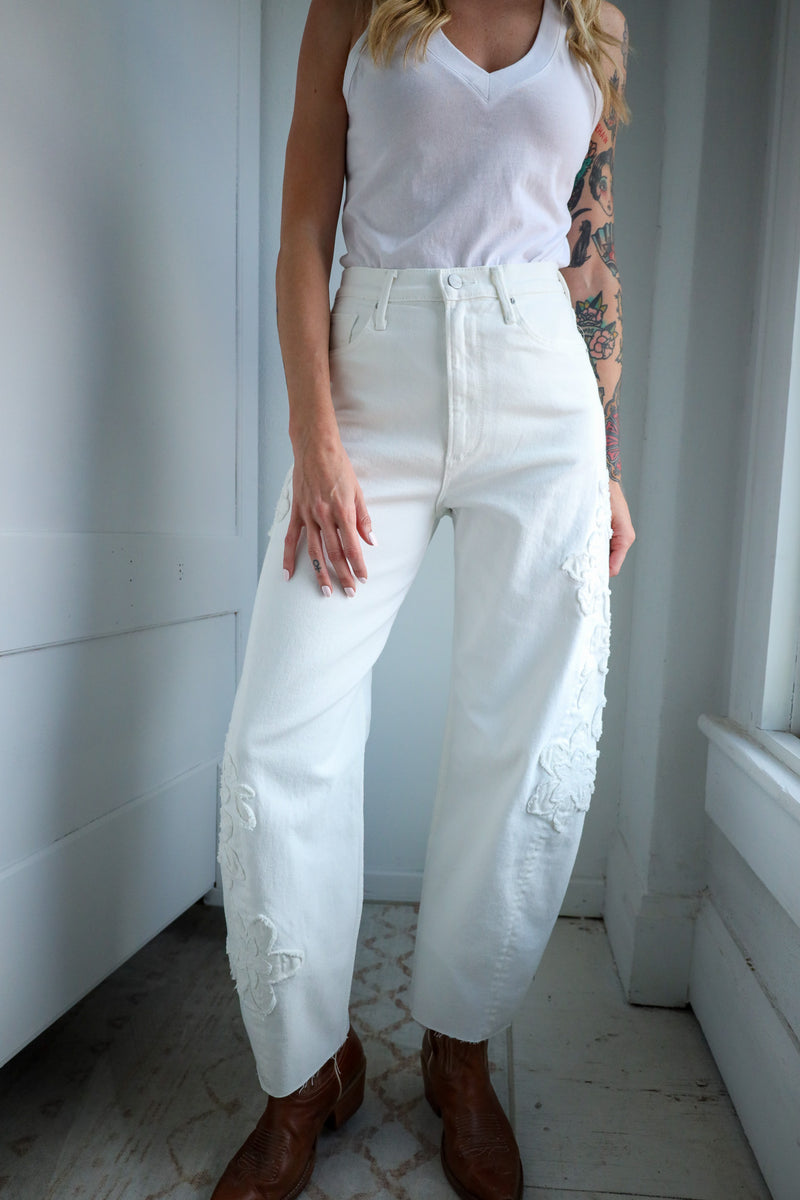 Person wearing a white sleeveless top and pants with brown boots indoors.