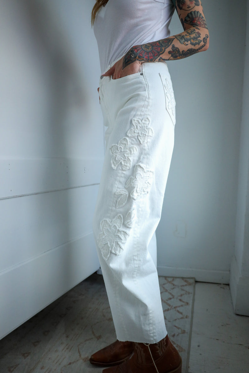Person wearing white pants with floral embroidery in a minimal indoor setting