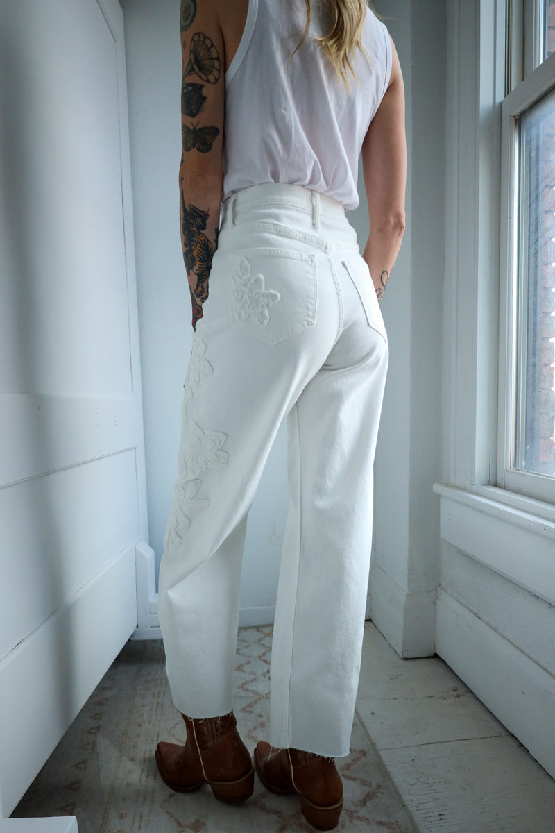 Person wearing white pants with floral embroidery in a room with a window.