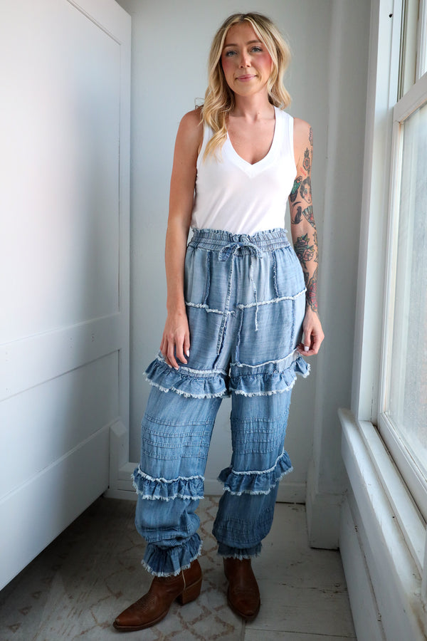 Woman wearing a white tank top and blue ruffled jeans standing indoors.