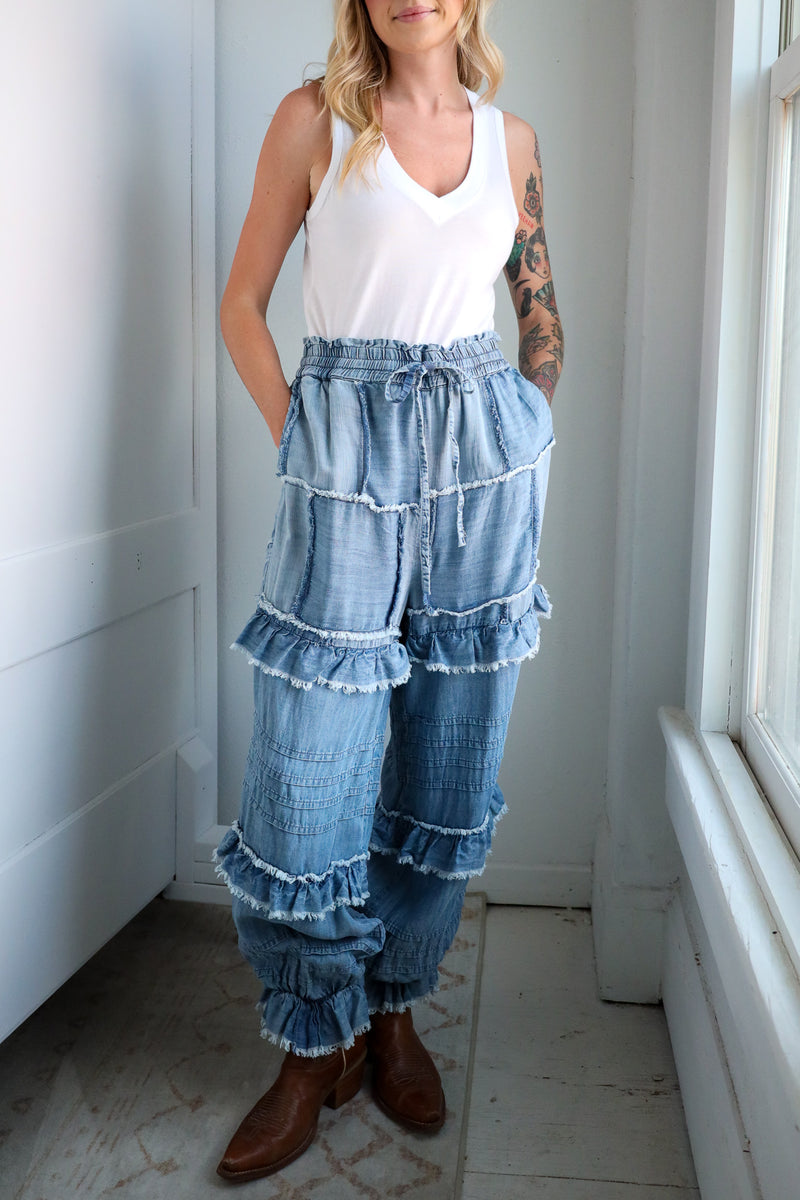 Woman wearing a white top and blue tiered denim pants in a room with a white door and window.
