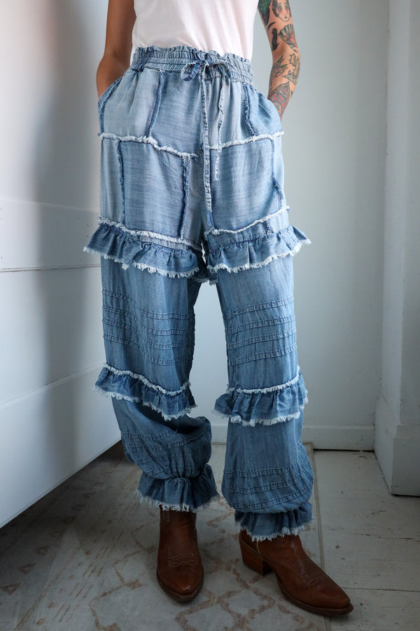 Person wearing layered denim pants with ruffles in a minimal indoor setting.