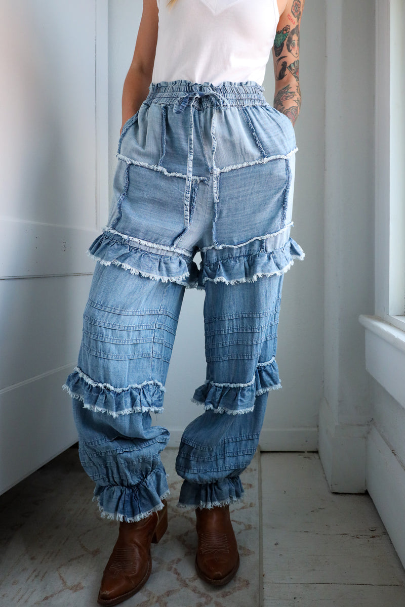 Person wearing denim ruffled pants with a white wall background