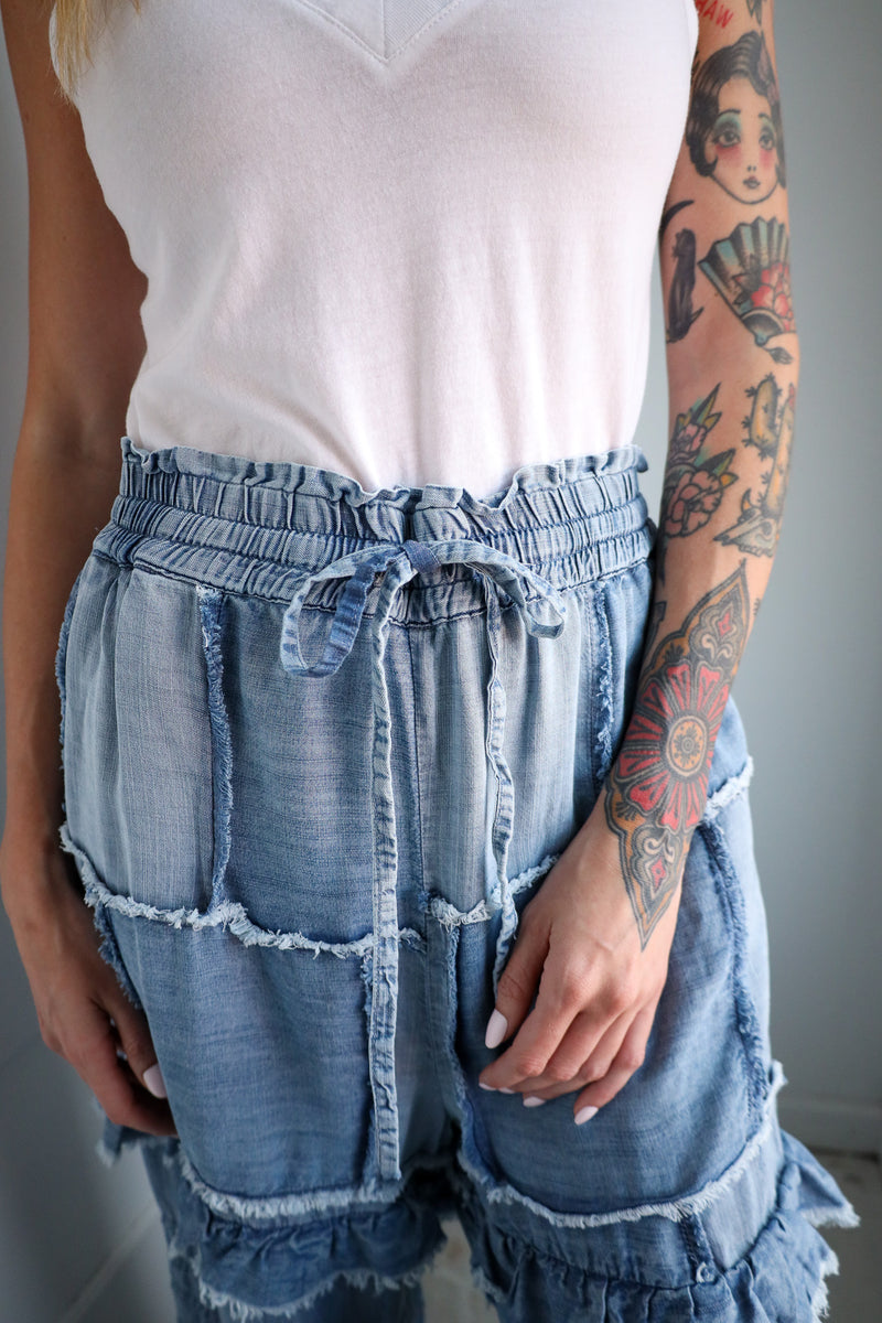 Person wearing a white top and blue denim shorts with ruffles, standing against a neutral background.