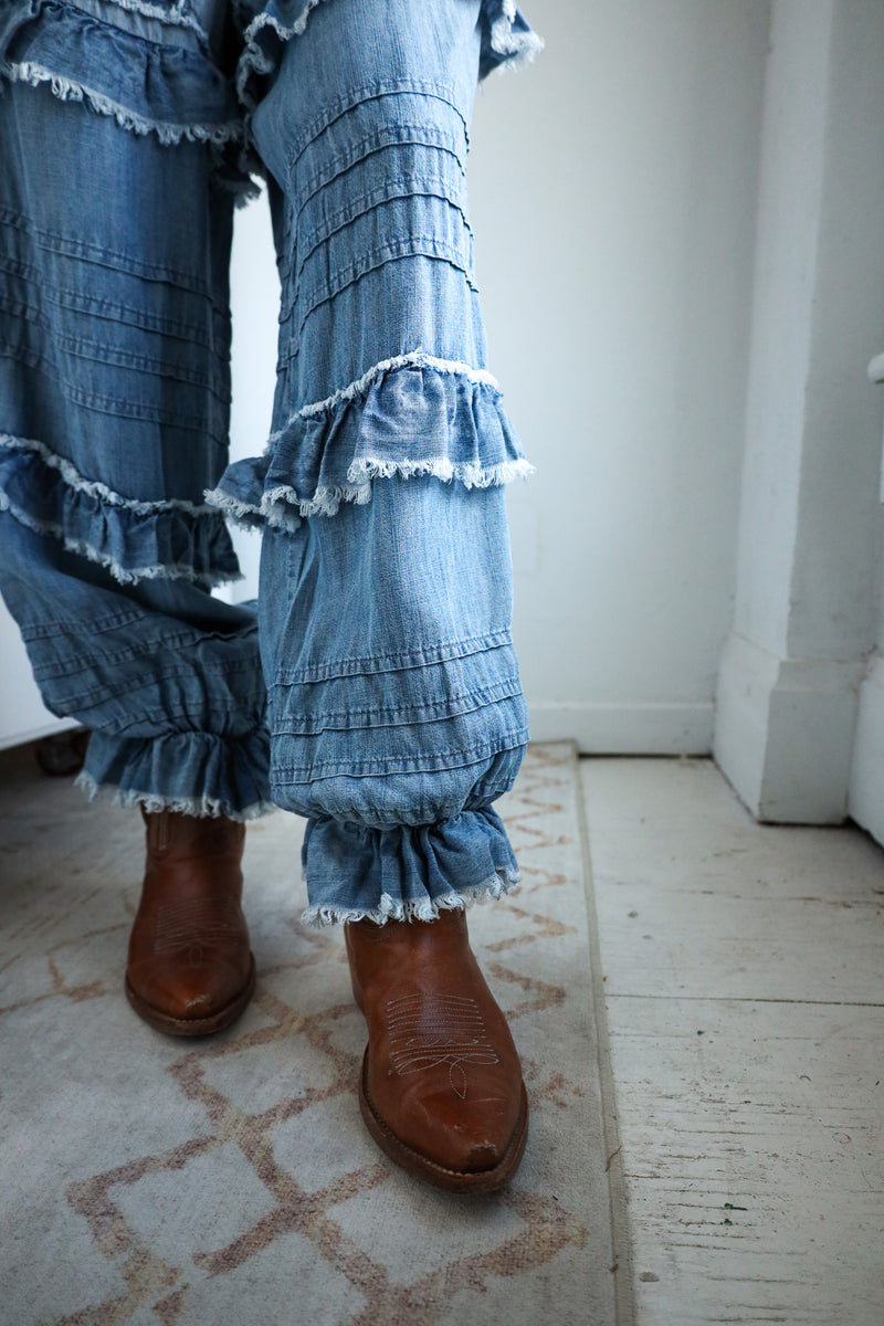 Denim pants with ruffles worn by a person on a patterned floor.