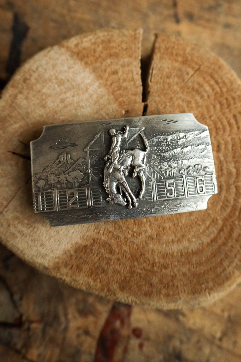 Silver belt buckle with a horse and rider design on a wooden surface