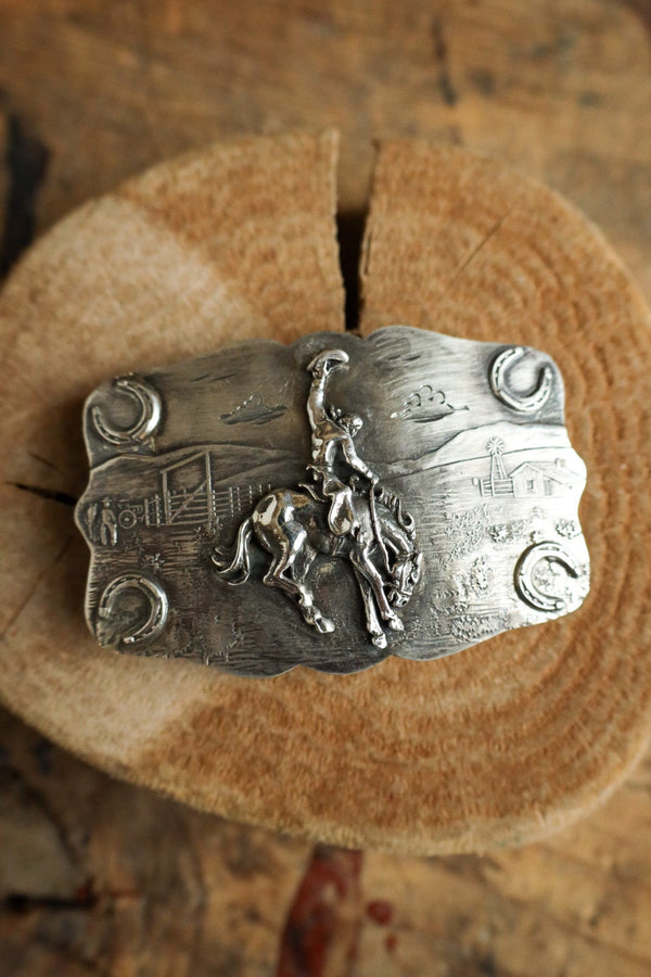 Silver belt buckle with horse design on a wooden surface