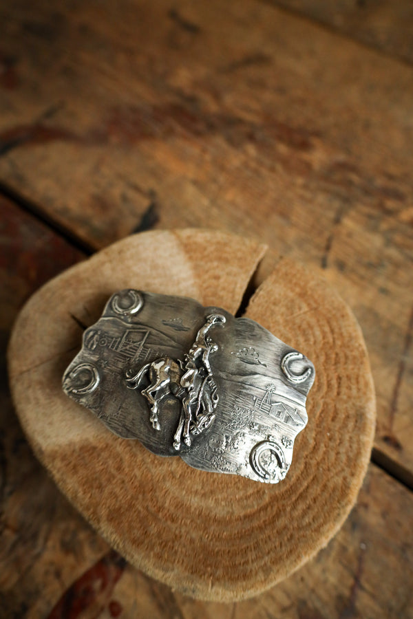 Silver pendant with a horse and rider design on a wooden surface
