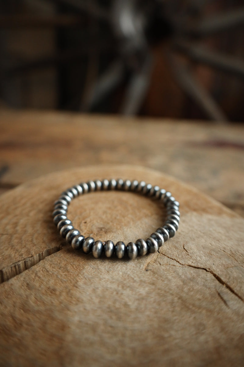 Silver beaded bracelet on a textured surface with a blurred background