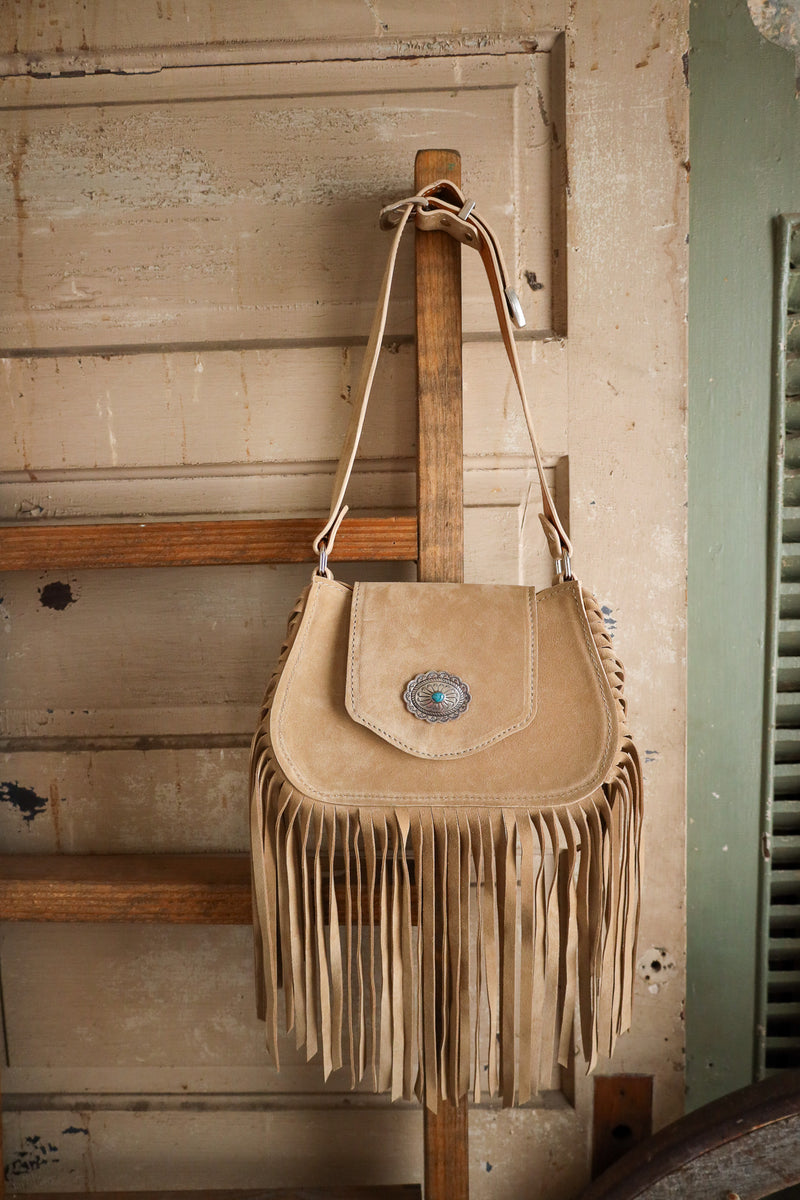 Beige fringe handbag hanging on a wooden ladder against a rustic wall.