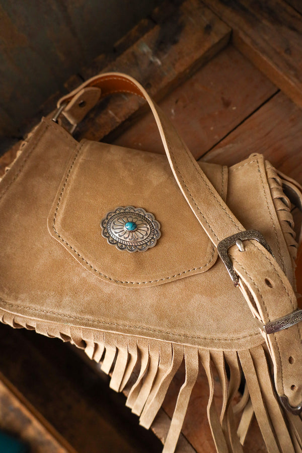 Brown leather bag with fringes and a decorative buckle on a wooden surface
