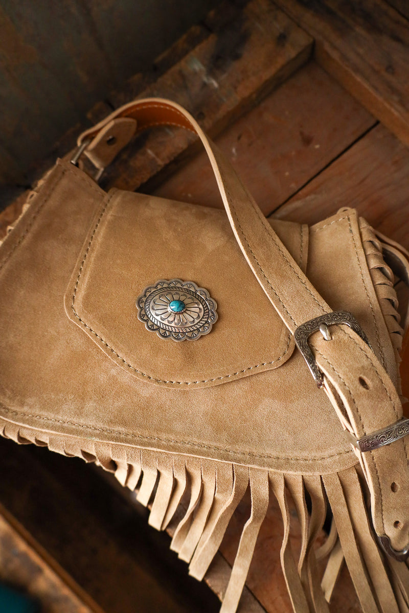 Brown leather bag with fringes and a decorative buckle on a wooden surface