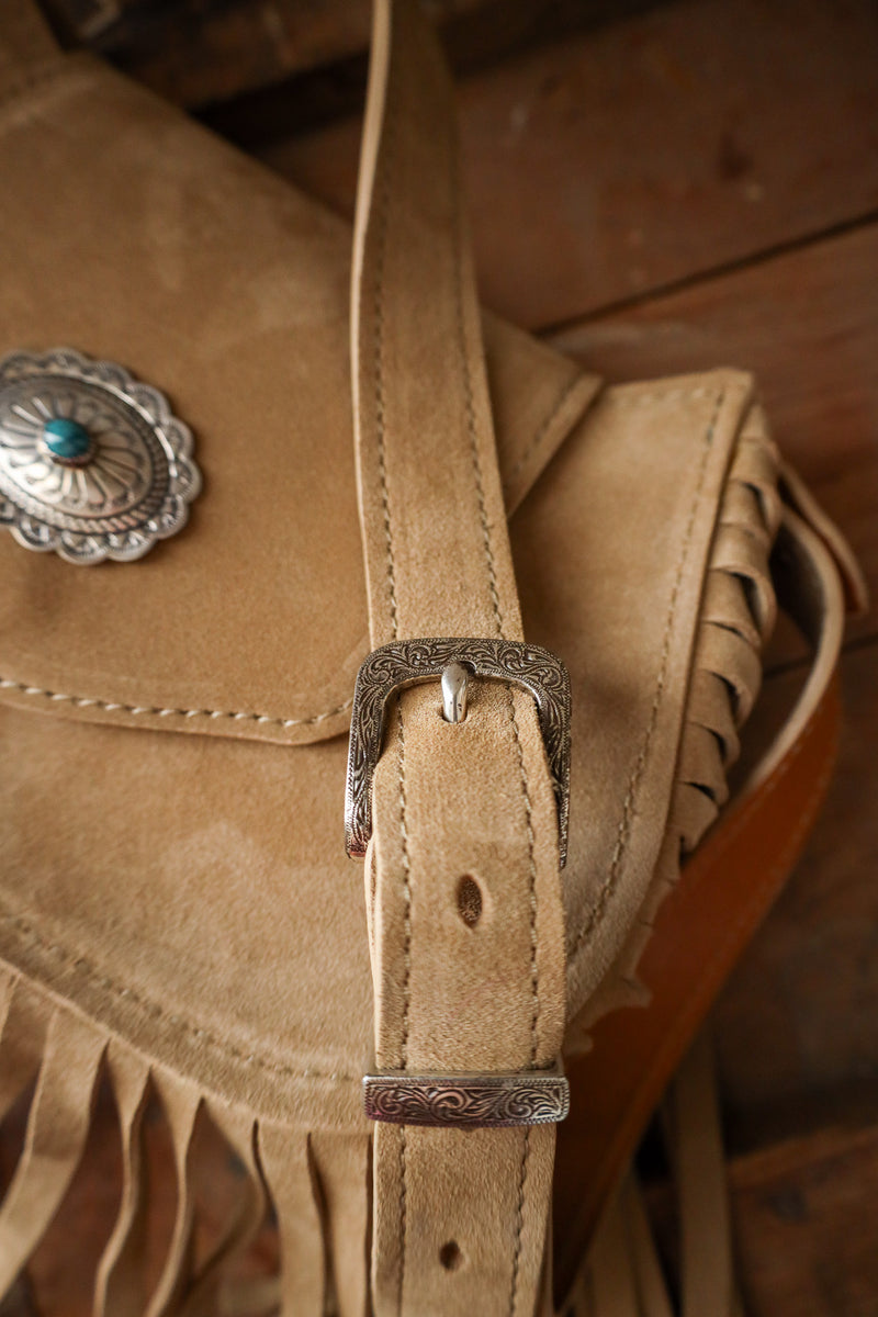 Close-up of a tan leather bag with fringe and metal buckle on a wooden surface