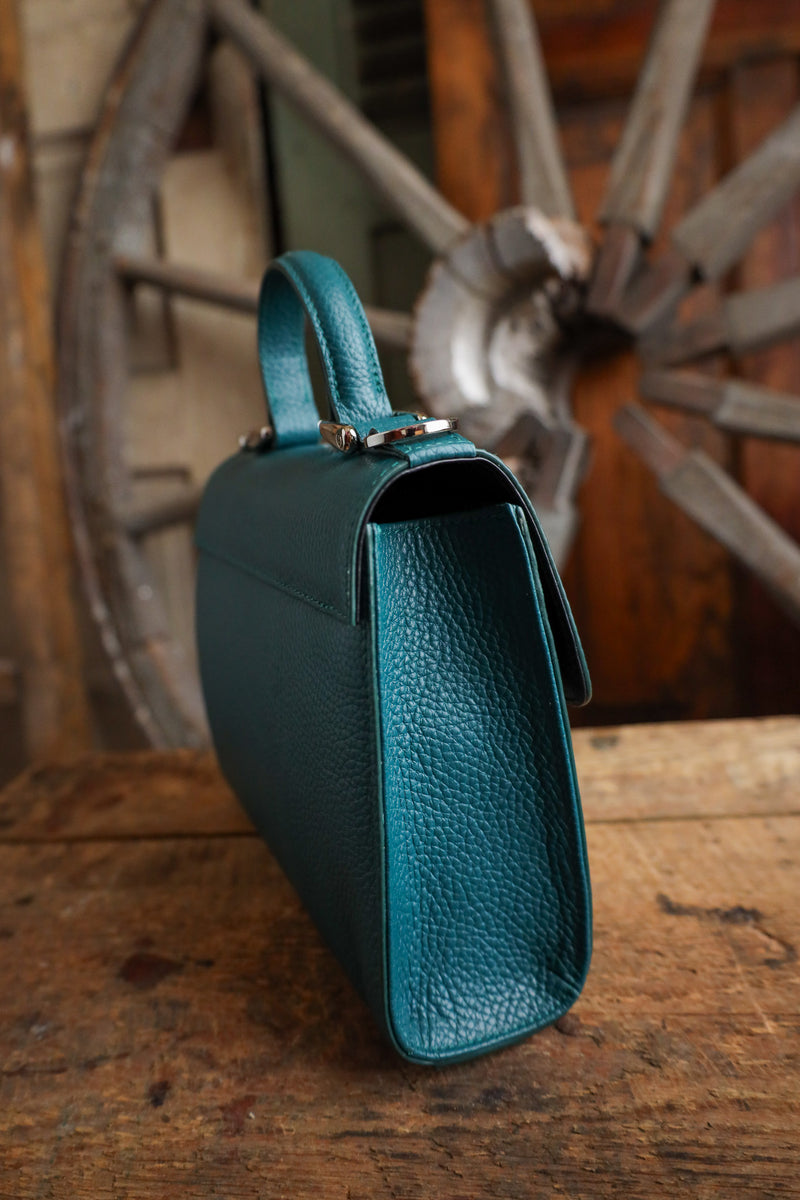 Teal handbag on a wooden surface with a rustic wheel in the background