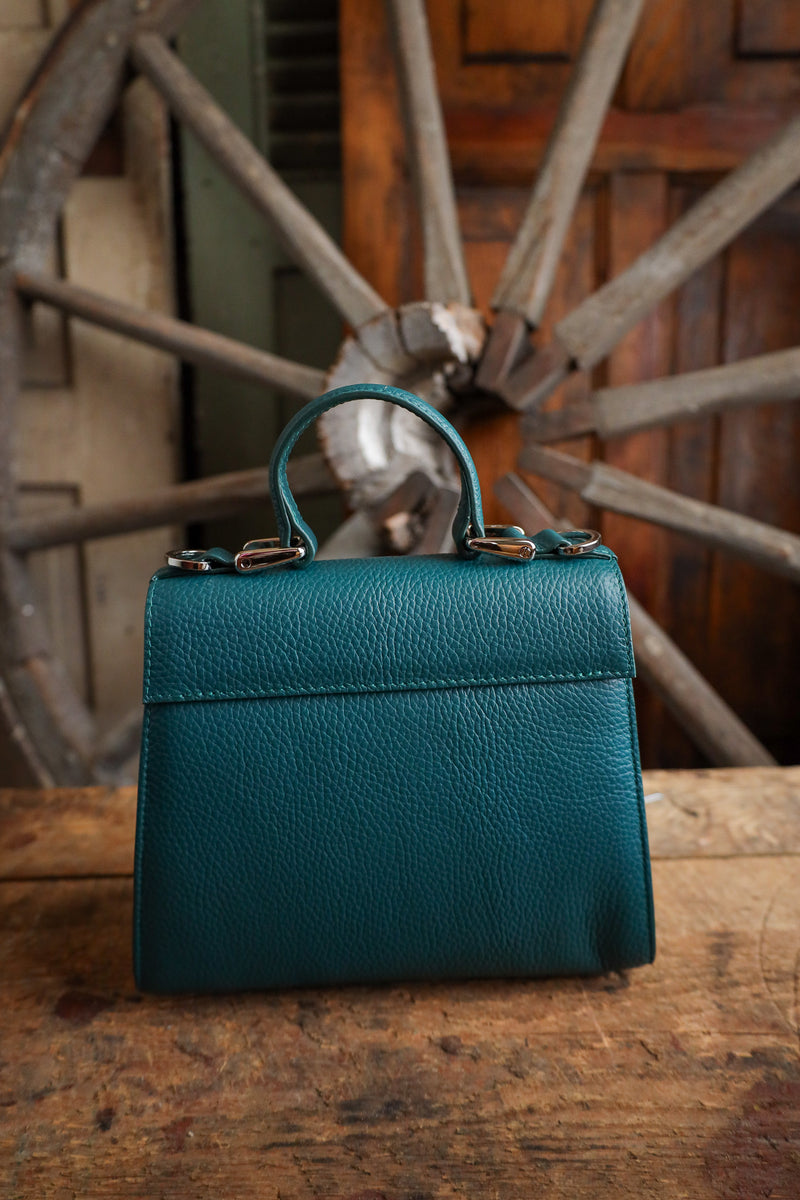 Teal handbag on a wooden surface with a rustic wheel in the background