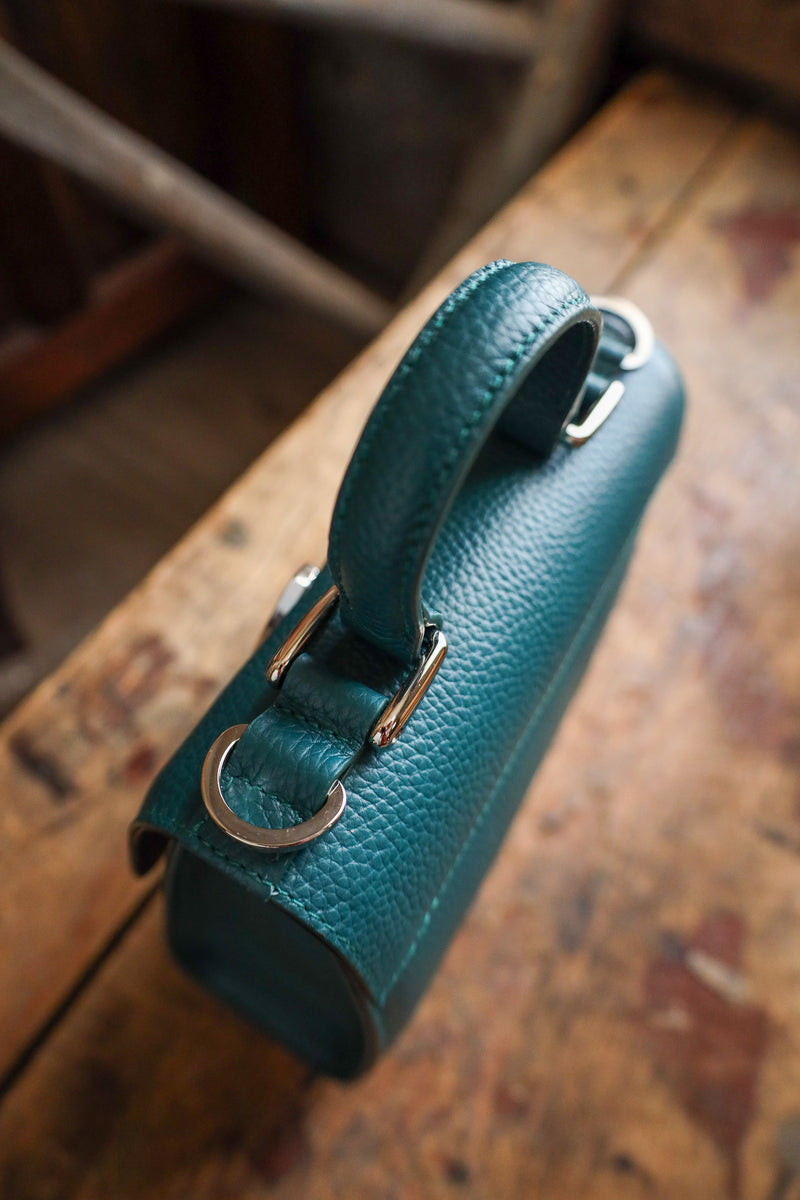 Teal handbag with silver buckle on a wooden surface