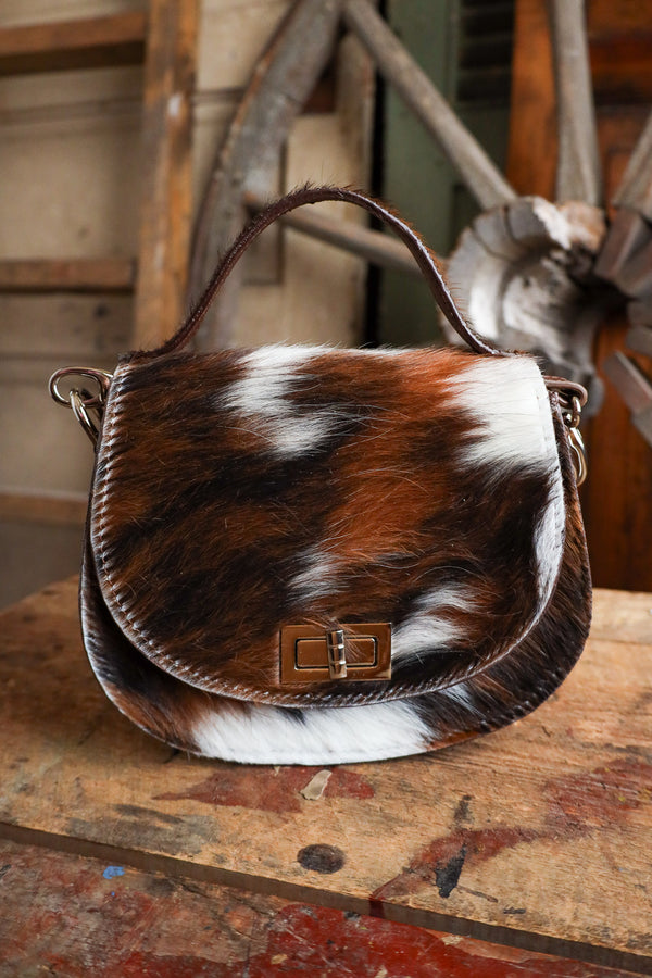 Brown and white cowhide leather bag on a wooden surface with rustic background