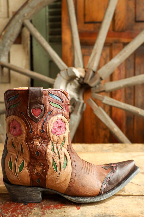 Decorative cowboy boot with floral patterns in front of a wooden wagon wheel.
