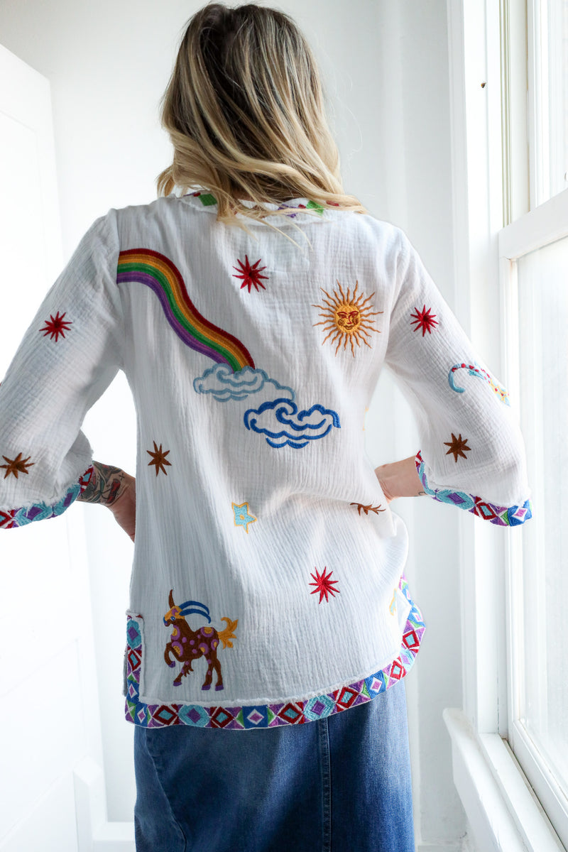 Person wearing a white embroidered shirt with colorful designs in a bright room.