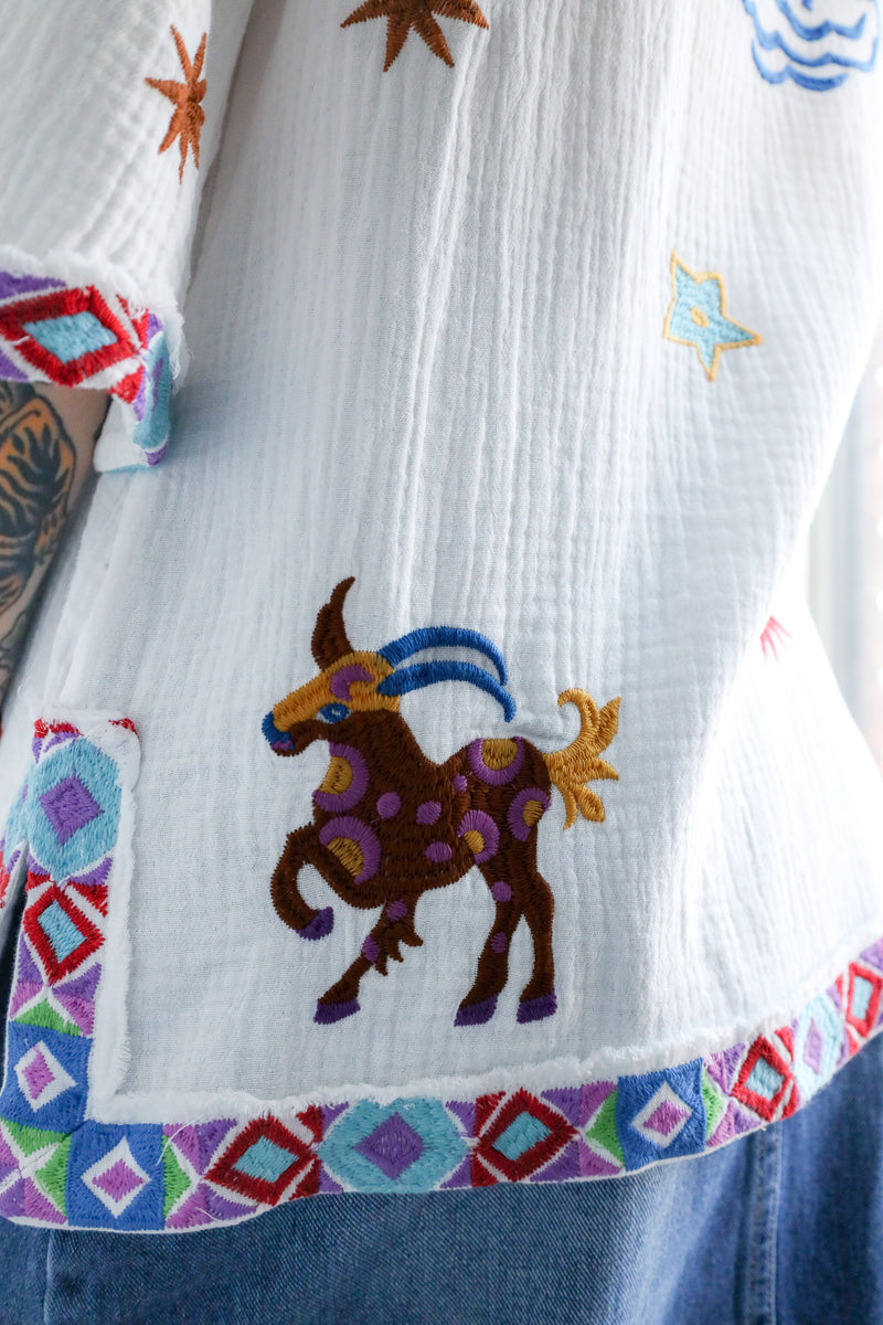 Embroidered fabric with a deer design and colorful geometric patterns on a white background.